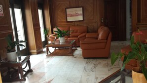 A lobby with a marble floor, leather sofas, a glass coffee table, and potted plants.