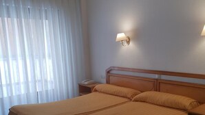 A double bed with a wooden headboard, a bedside table with a lamp, and a window with sheer curtains.