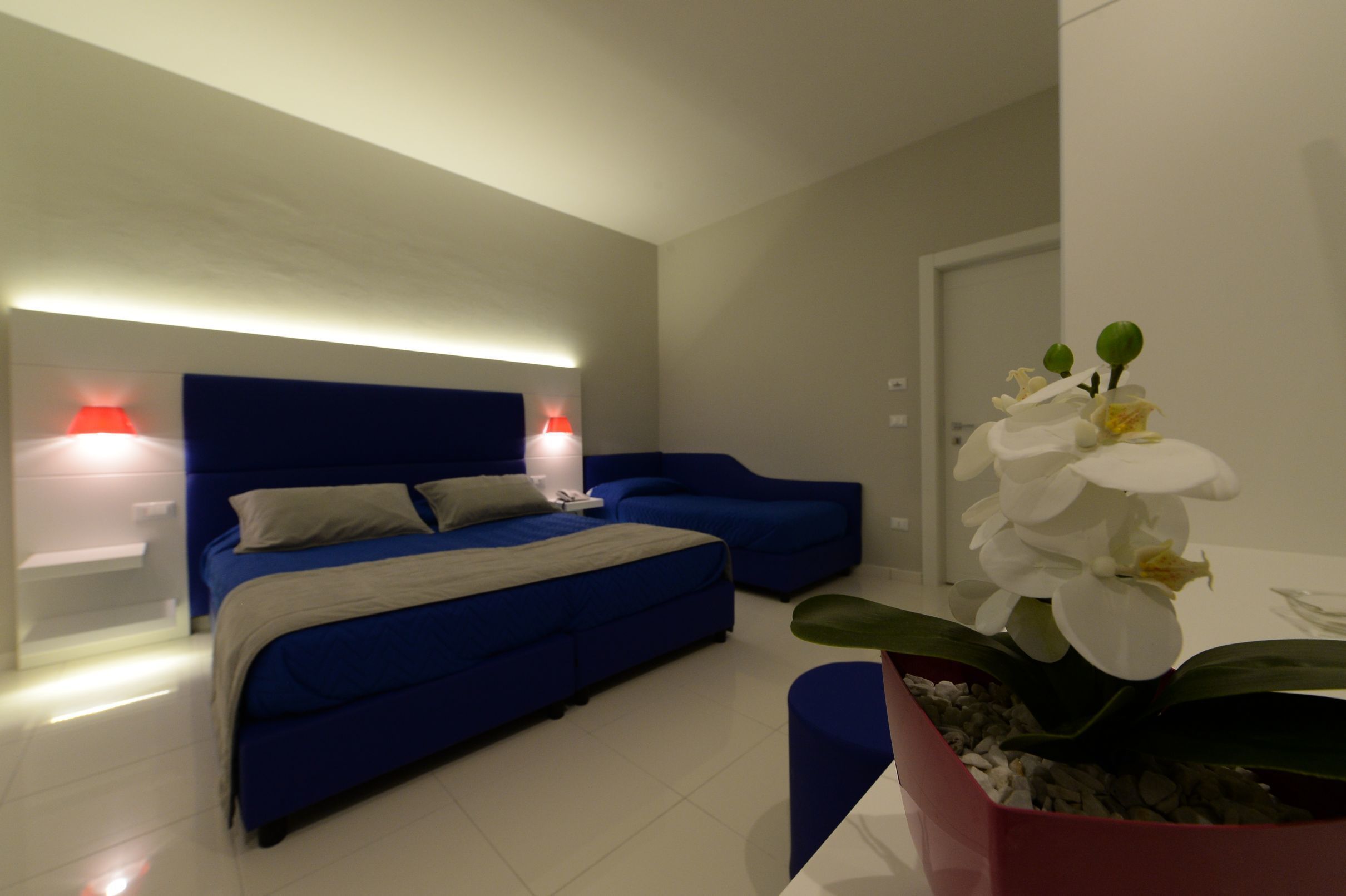 Une chambre moderne avec un lit bleu, des tables de chevet et une orchidée en pot.