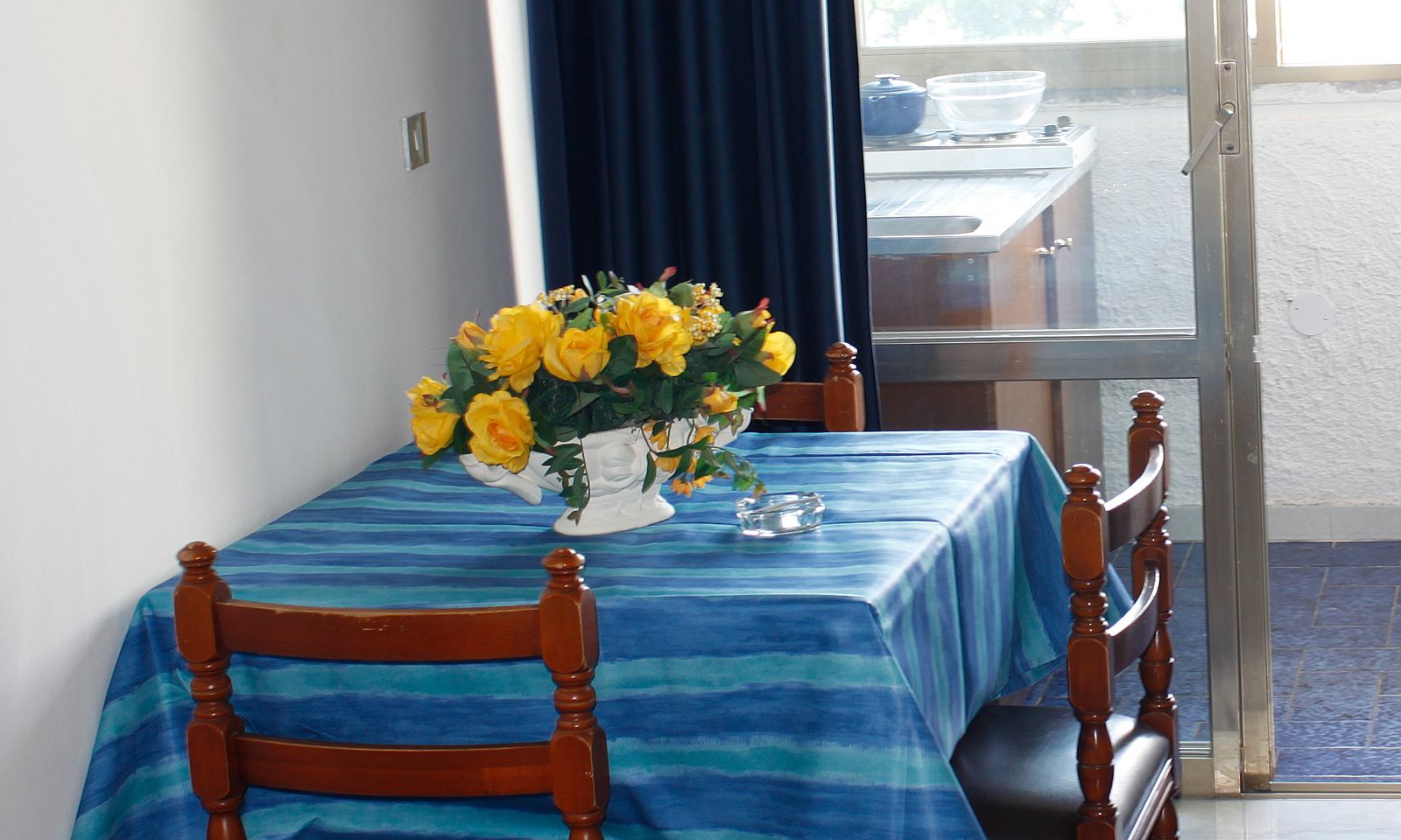 Et spisebord med et blåt dug, en vase med gule blomster og en glasaskebæger.