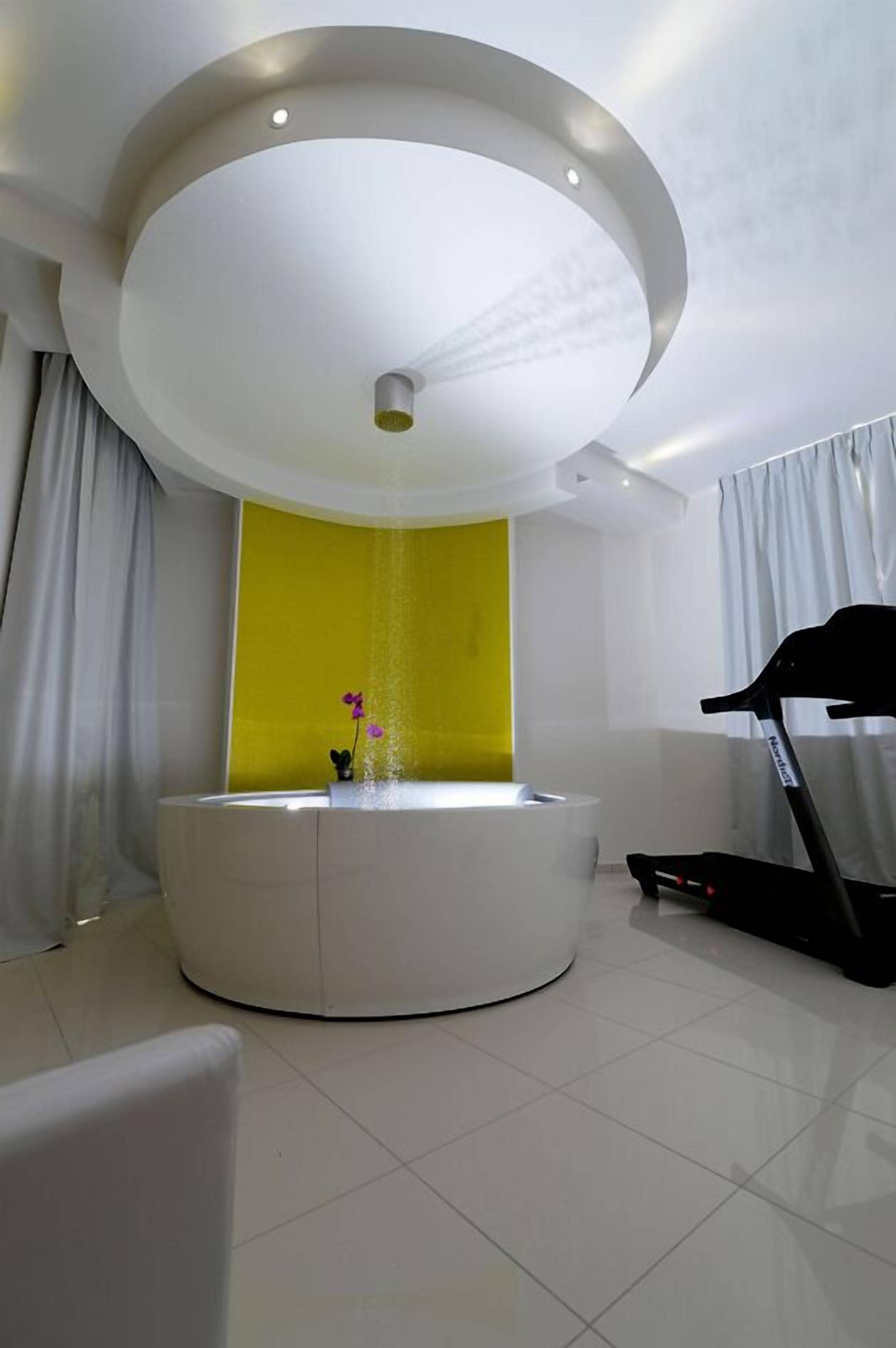 A modern bathroom with a circular sink, a treadmill, and a yellow accent wall.
