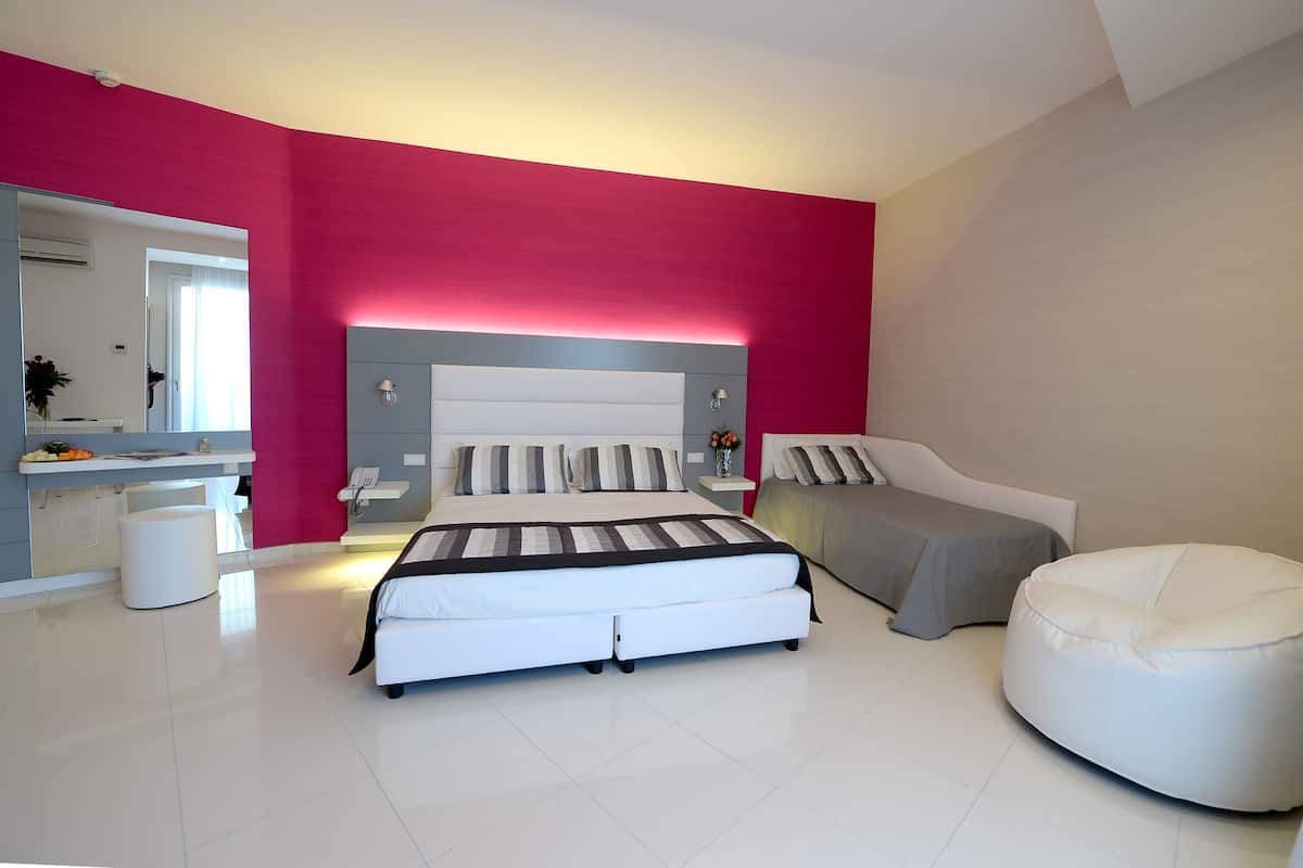 Une chambre à coucher moderne avec un grand lit, des tables de chevet, une coiffeuse et un fauteuil en forme de poire de couleur blanche.