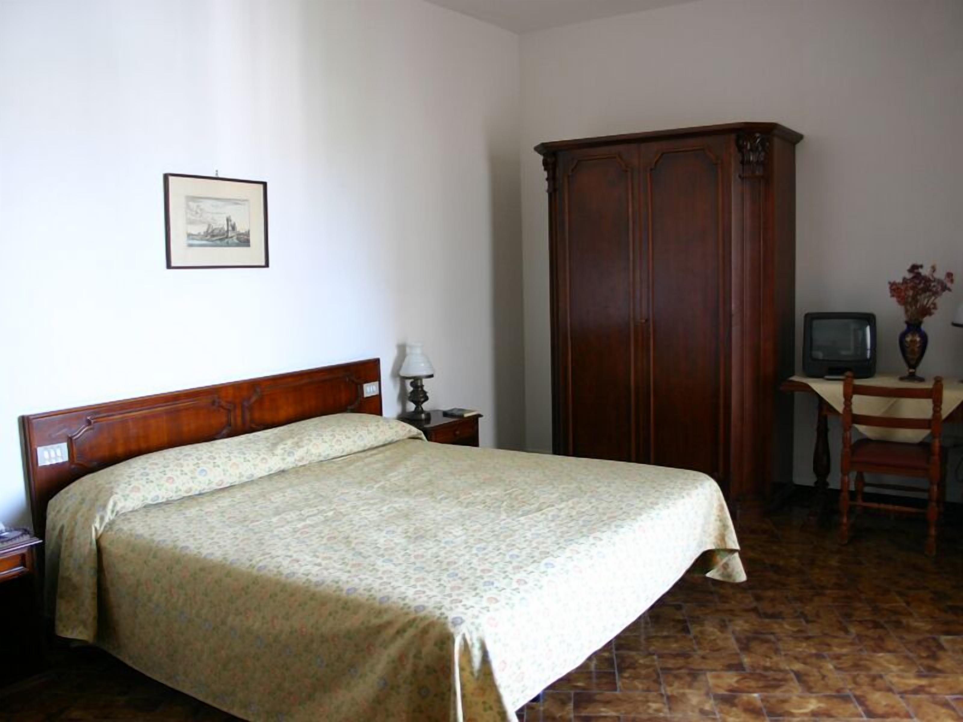 Un dormitorio con cama, un armario de madera, un escritorio con silla, televisión y un cuadro en la pared.