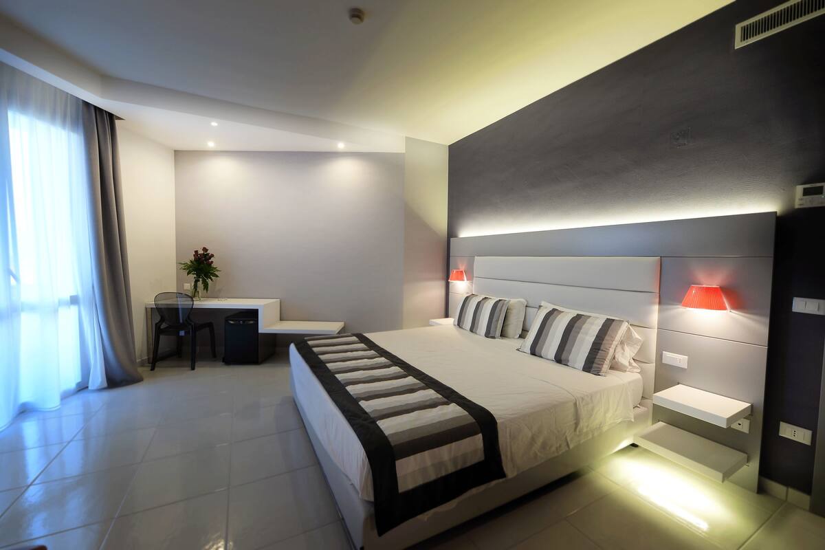 Une chambre d’hôtel moderne avec un grand lit, des tables de chevet, un bureau avec une chaise et une plante en pot.