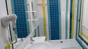 Une salle de bain avec un lavabo blanc, un miroir, un sèche-cheveux et une douche dont les carreaux sont bleus et jaunes.