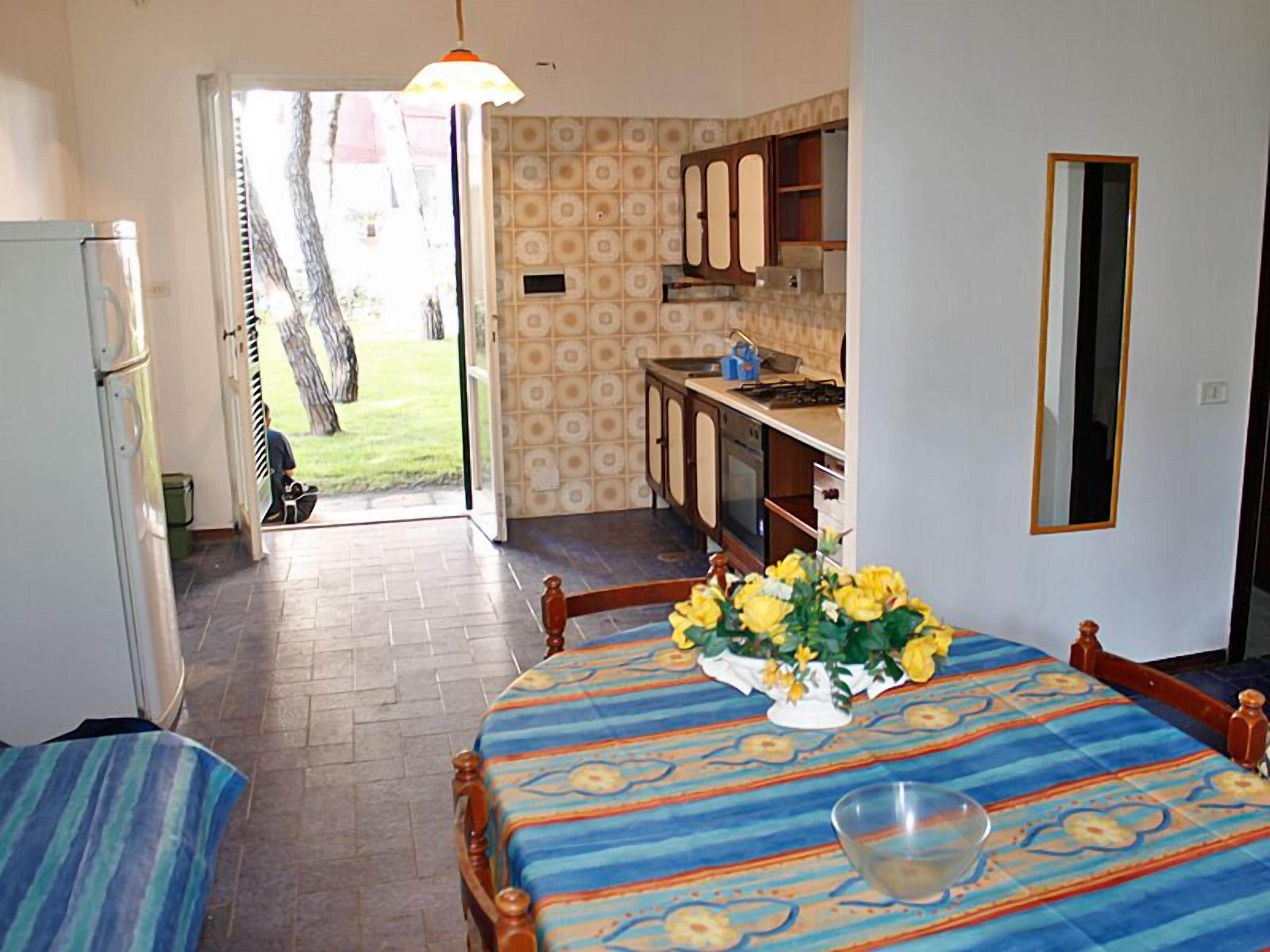 A room with a dining table, a kitchen area, and a view of the outdoors.
