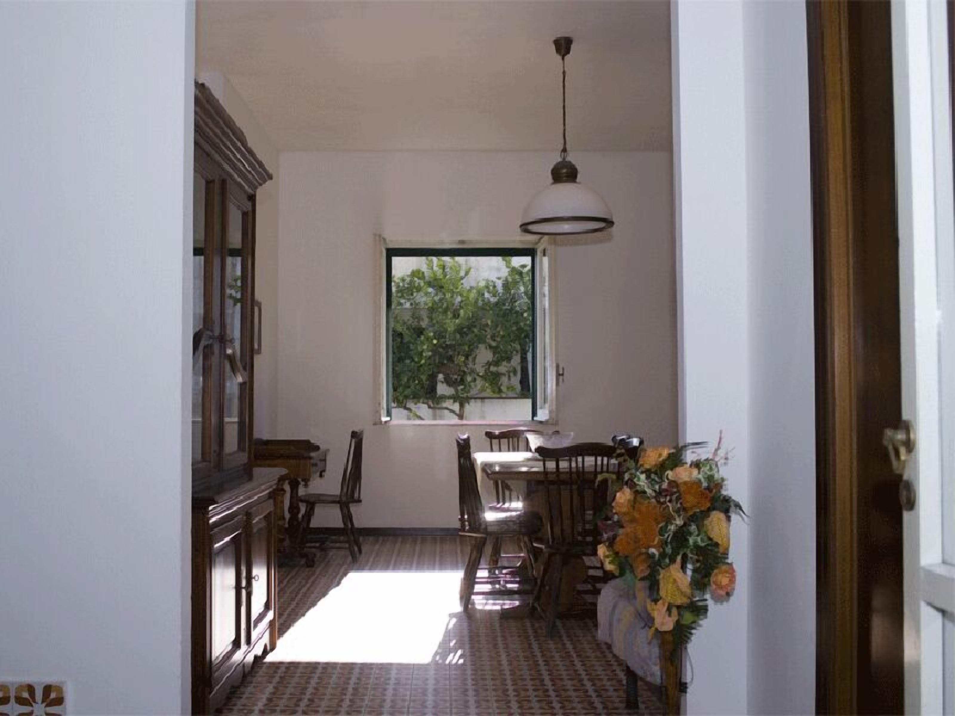 Un pasillo estrecho con un comedor, una ventana que da a zonas verdes y una lámpara colgante.