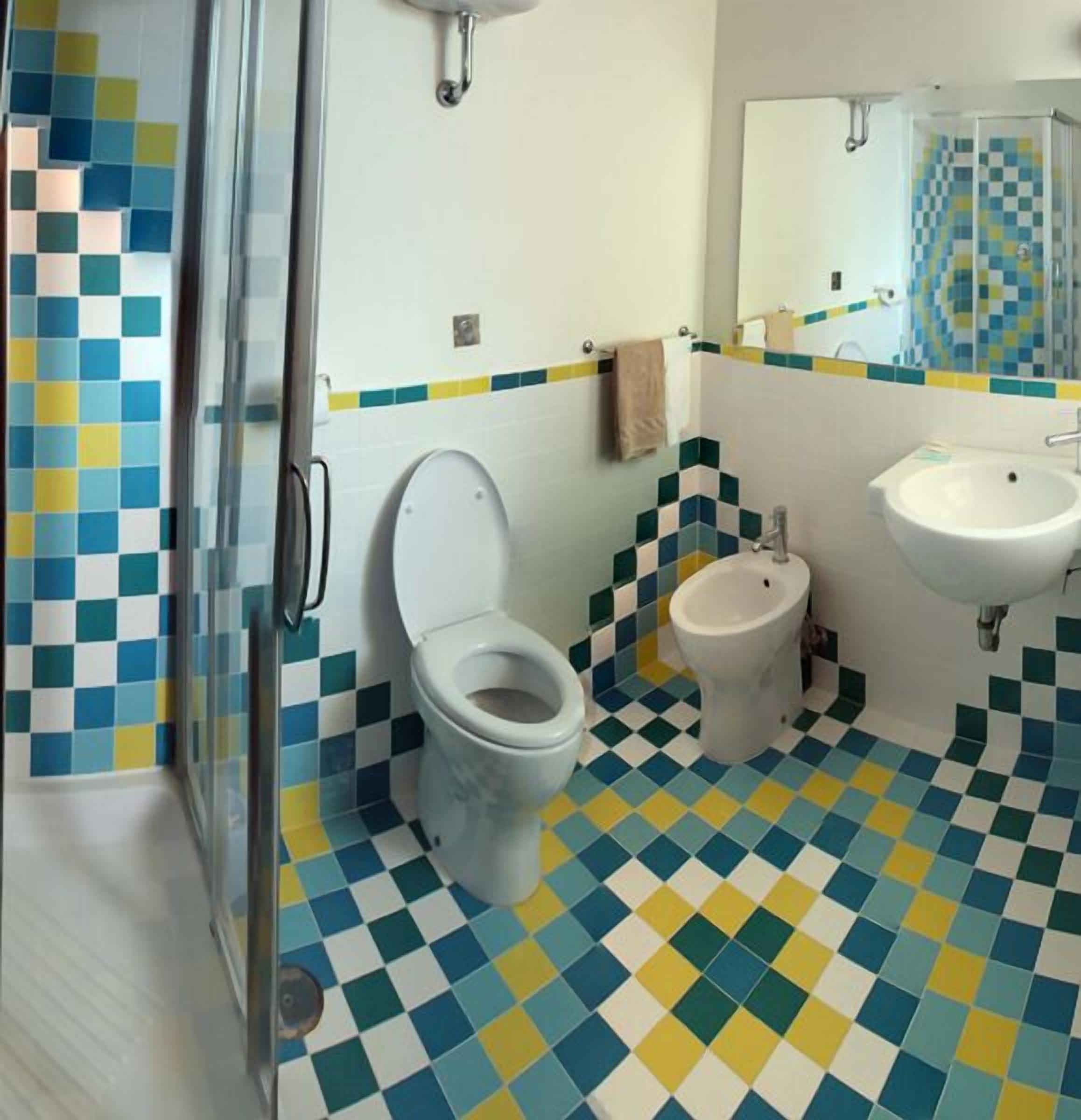 Ein Badezimmer mit Schachbrettboden, Toilette, Waschbecken und Duschbereich.