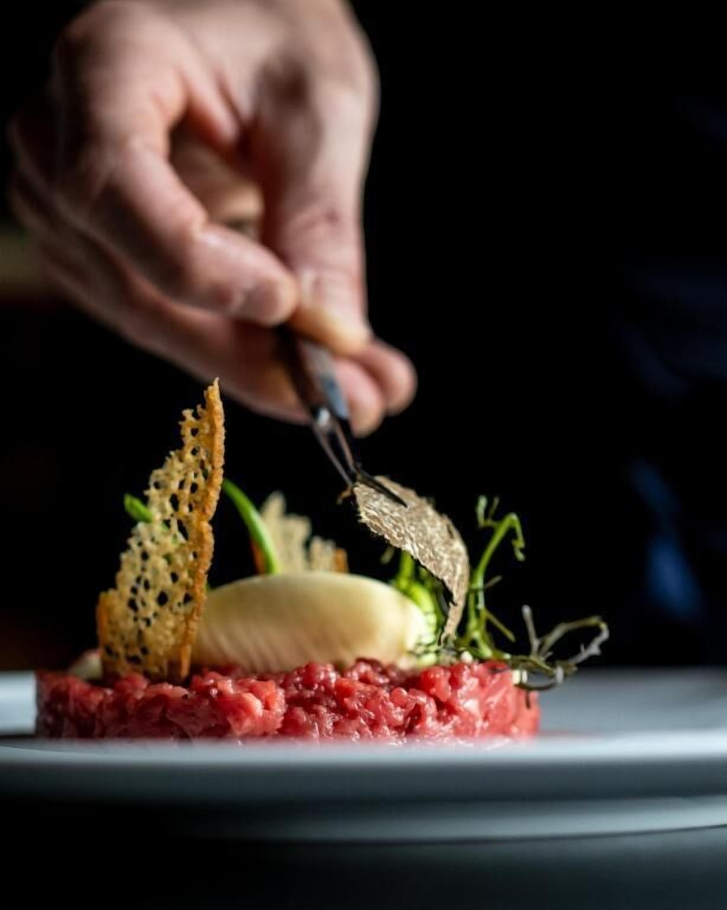 Una mano cortando un plato con carne, un vegetal y algunas guarniciones.