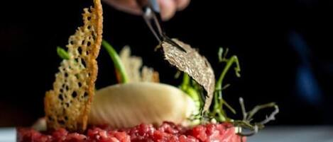 Una mano cortando un plato con carne, un vegetal y algunas guarniciones.