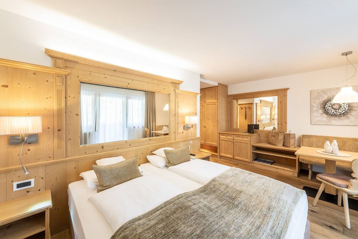 A hotel room with a large bed, wooden furniture, a desk, and a mirror.