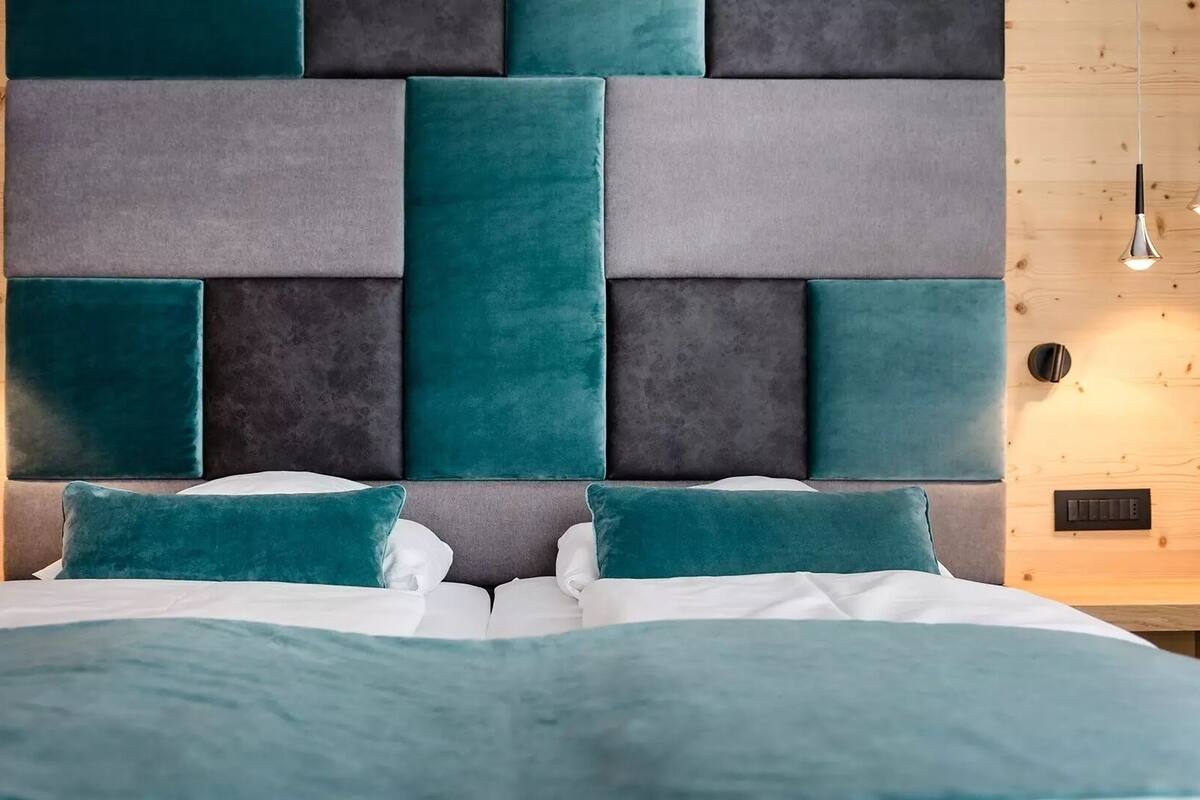 A bedroom with a modern headboard, a bed with white bedding, and two bedside tables with lamps.