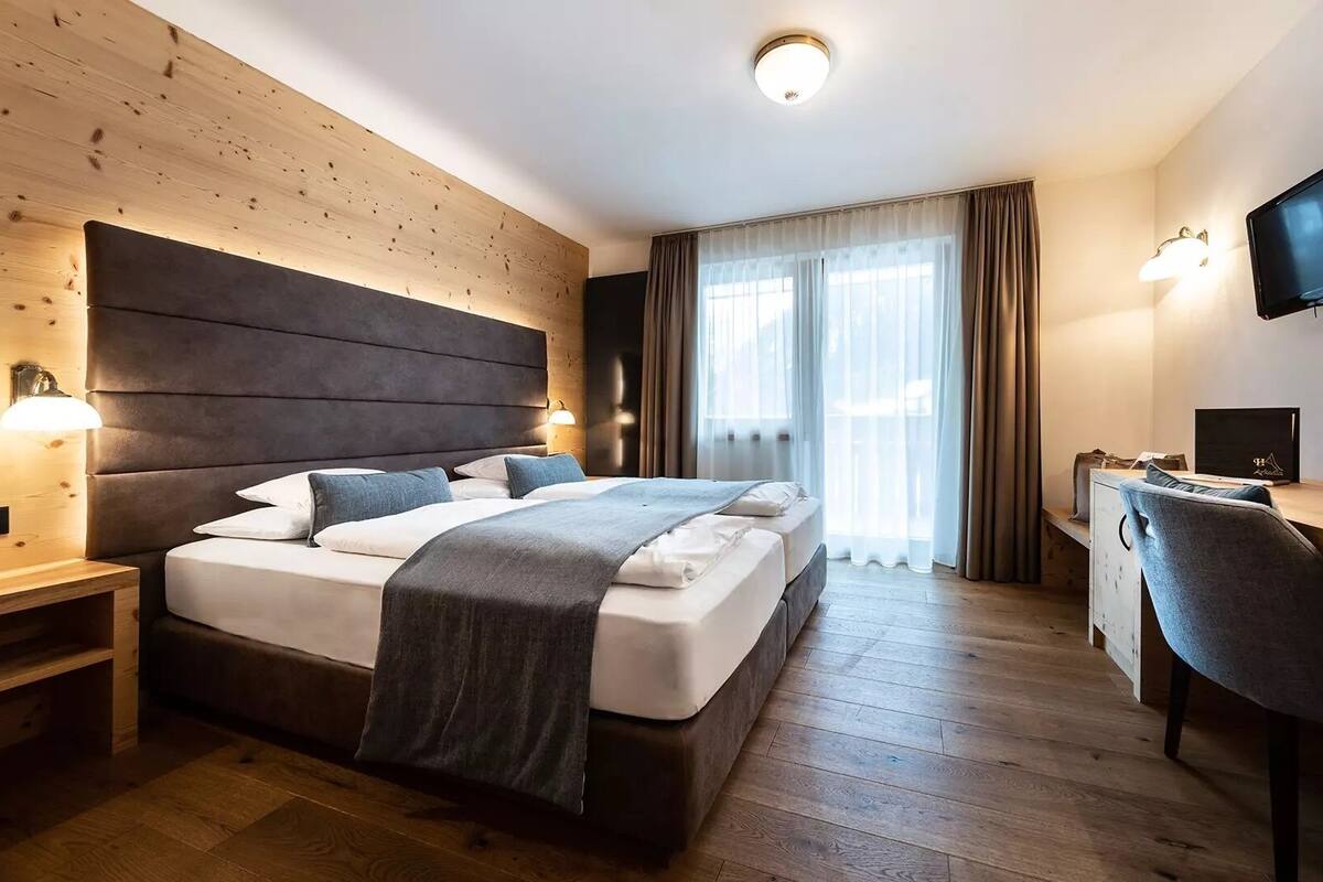 A hotel room with a large bed, a desk, a chair, a TV, and a window with curtains.