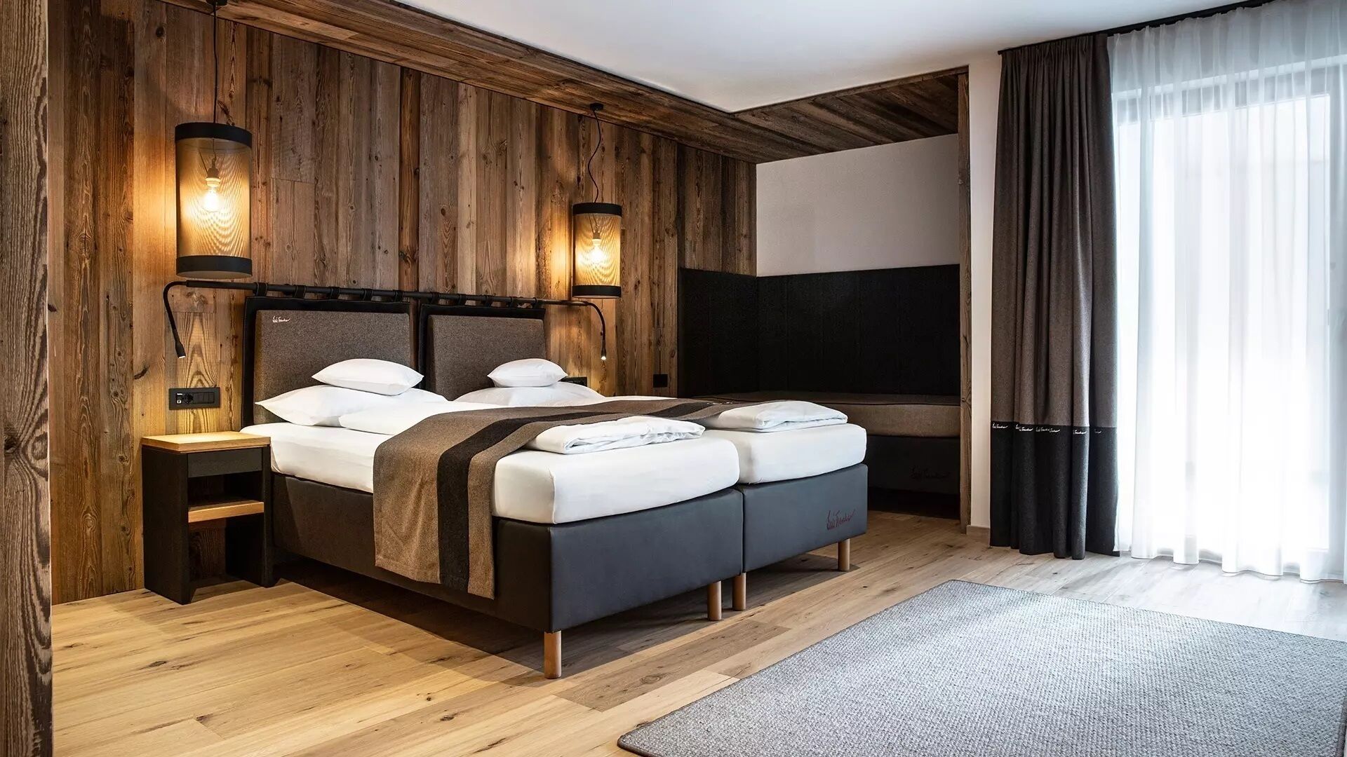 Ein modernes Schlafzimmer mit einer Holzvertäfelung, einem großen Bett mit Kopfteil, Nachttischen und einem Fernseher.