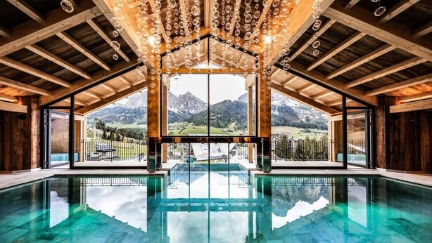 A large indoor swimming pool with a view of mountains through large windows. - Hotel Arkadia - Adults Only (Corvara in Badia)