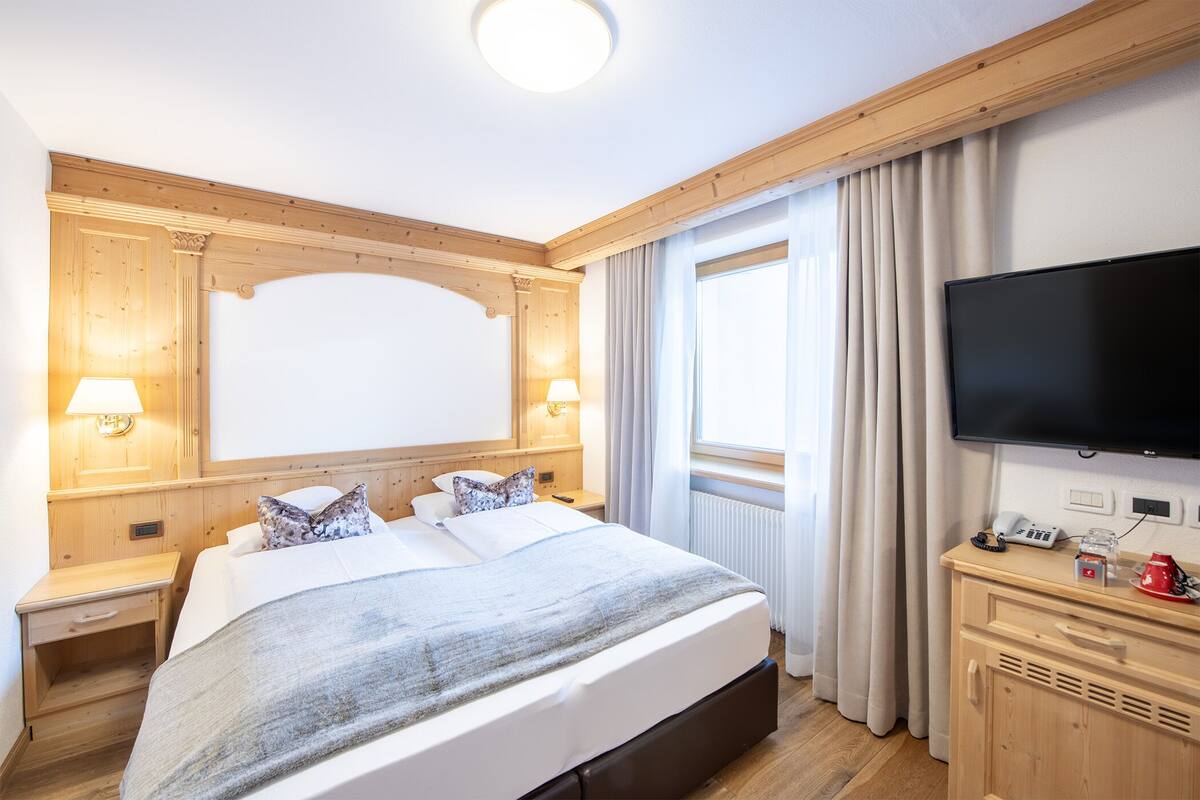 A hotel room with a large bed, two bedside tables with lamps, a TV, and a wooden cabinet.