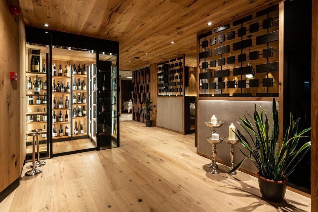 A wooden interior with shelves of wine bottles, a plant, and candle holders.