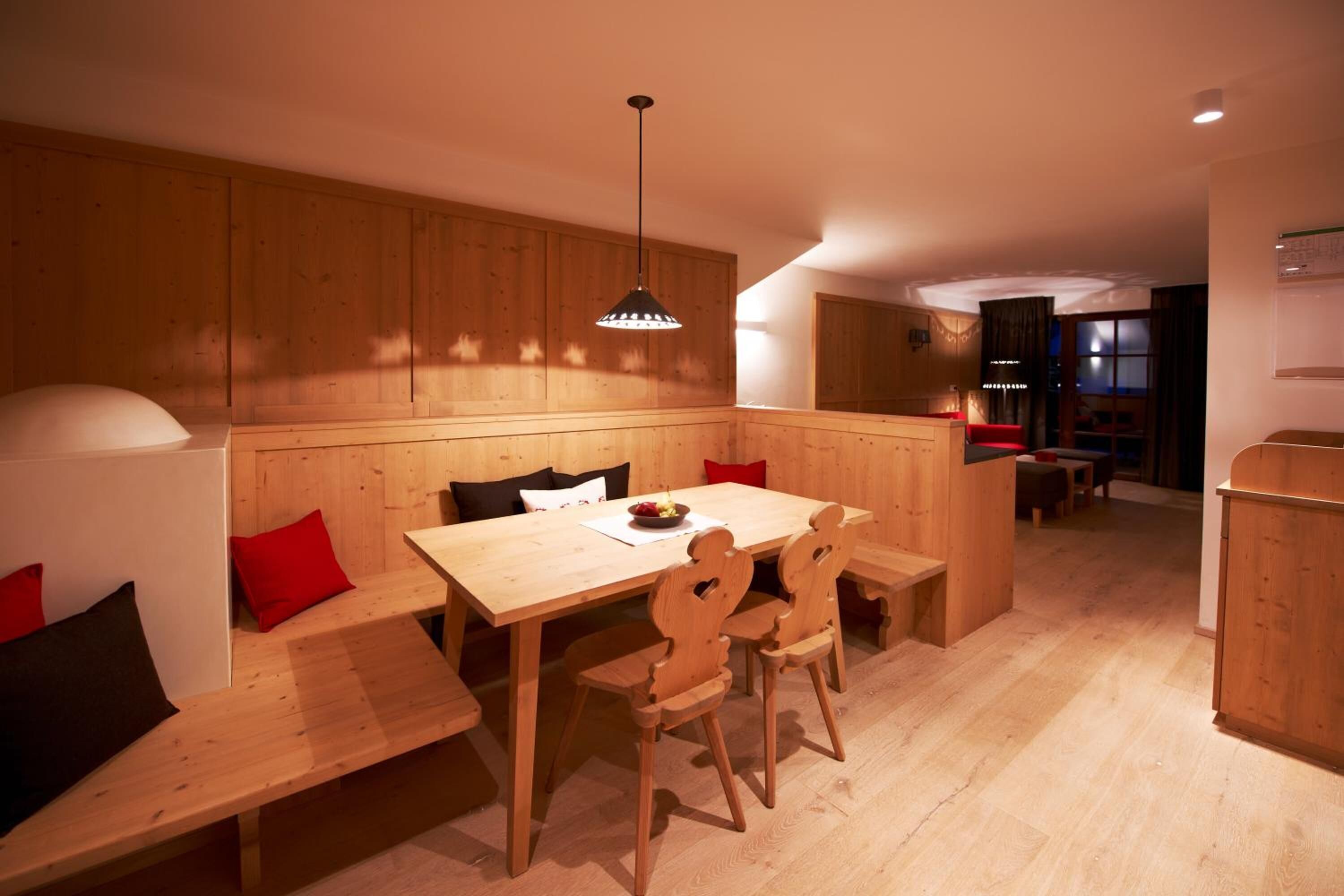 A cozy dining area with a wooden table and benches, a hanging light fixture, and a view into another room.