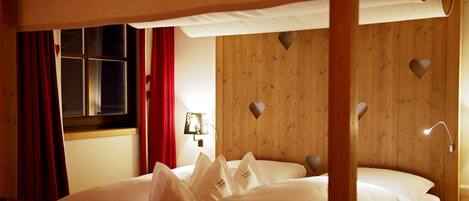 Quarto de madeira com cama, cortinas vermelhas e recortes em formato de coração na parede.