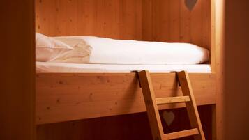 Ein Holzbett mit Etagen und einer Leiter, ein herzförmiges Loch in der Wand sowie ein weißes Bettlaken.