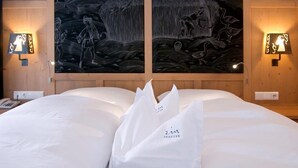A hotel room with a bed, two wall-mounted light fixtures, and two large wall paintings. - Zin Senfter Residence (San Candido)