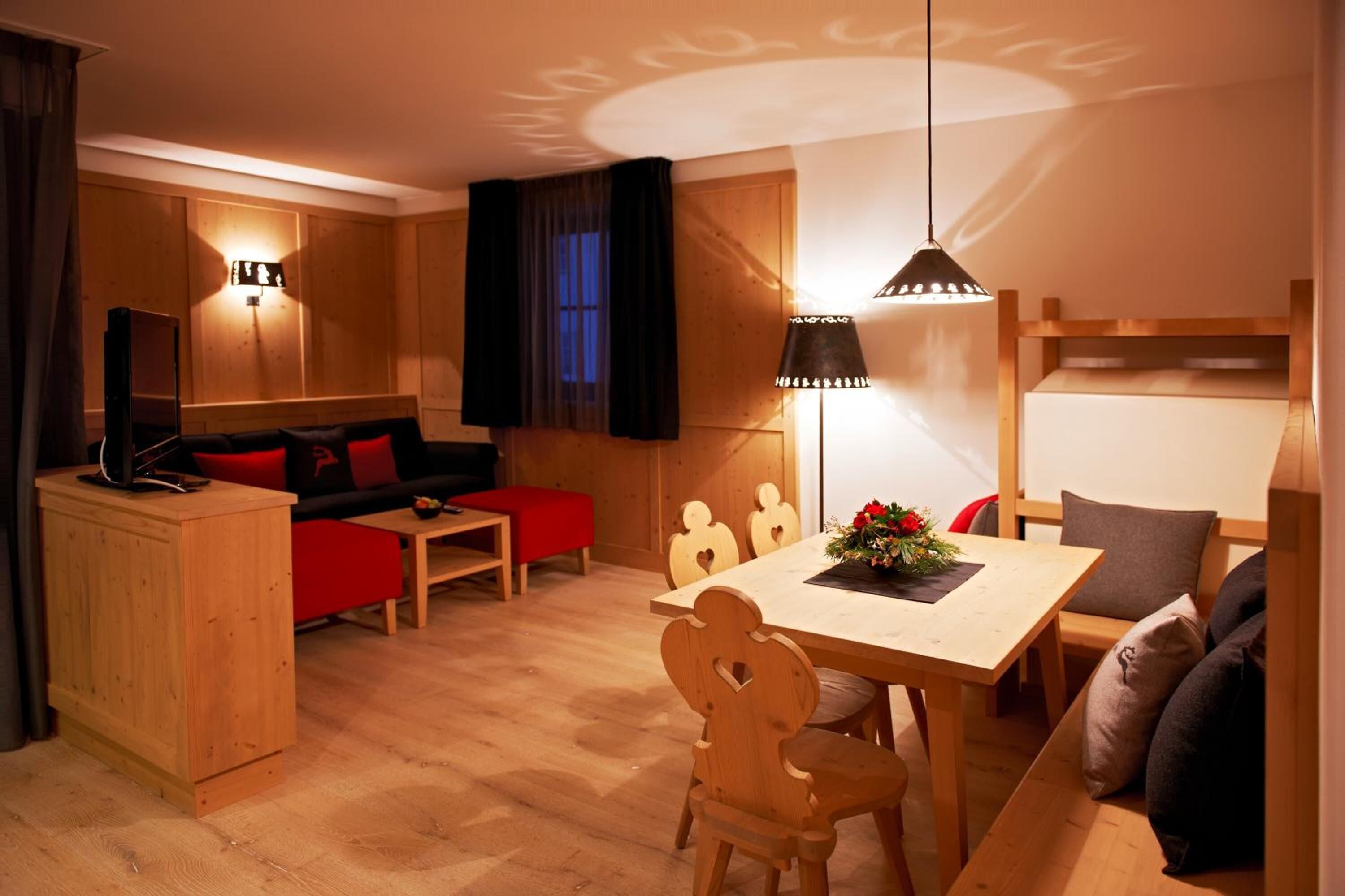 A cozy room with a wooden dining table, a sofa, a TV, and a wall-mounted lamp.
