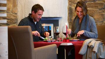 Een eettafel met twee personen aan het eten, een open haard en stenen muren.