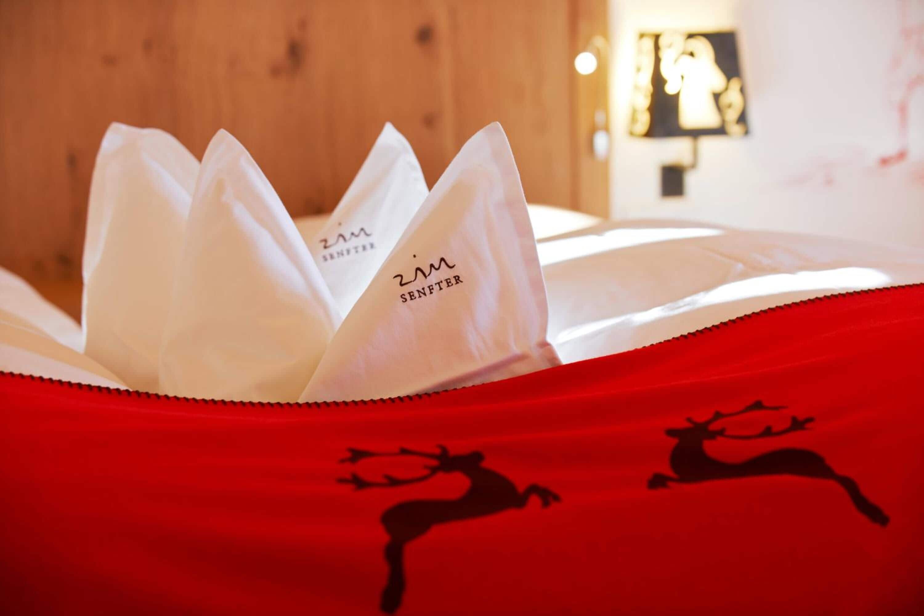 Una cama con una colcha roja que muestra siluetas de renos y un almohadón blanco con el texto 'ZIM SENFTER'.