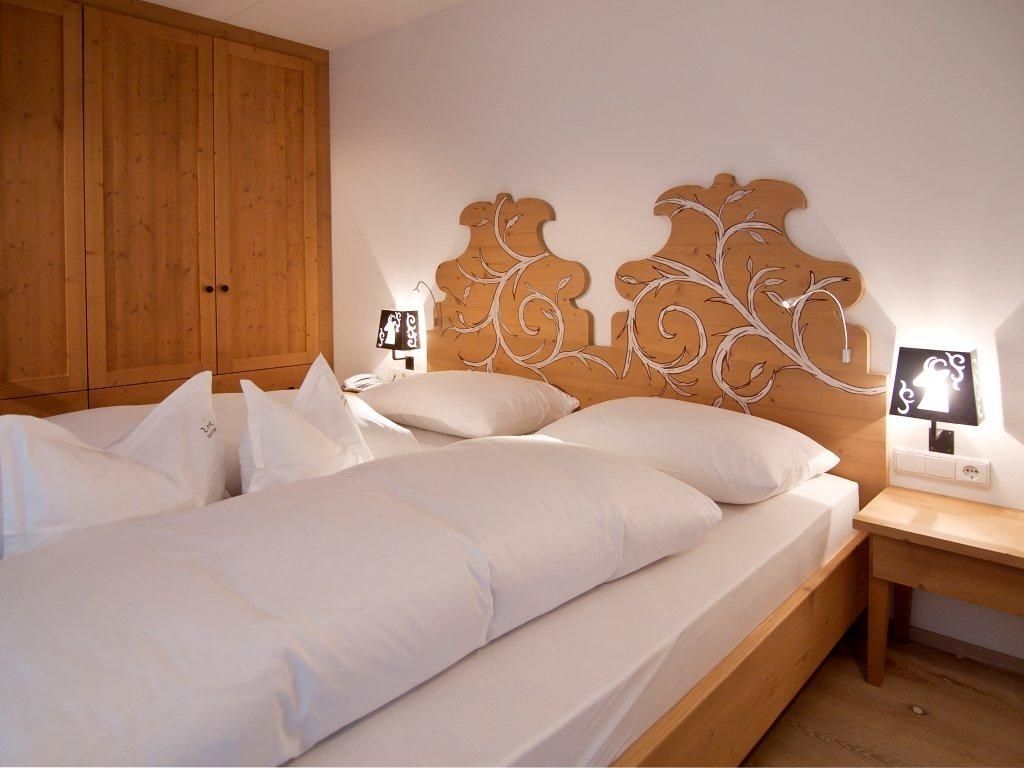 A double bed with white linens, a wooden headboard with a leaf design, and bedside tables with lamps.