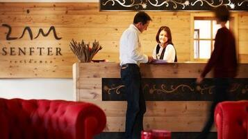 A reception desk with a wooden backdrop and the name "SENFTER residence" visible. There are red upholstered chairs in the foreground.