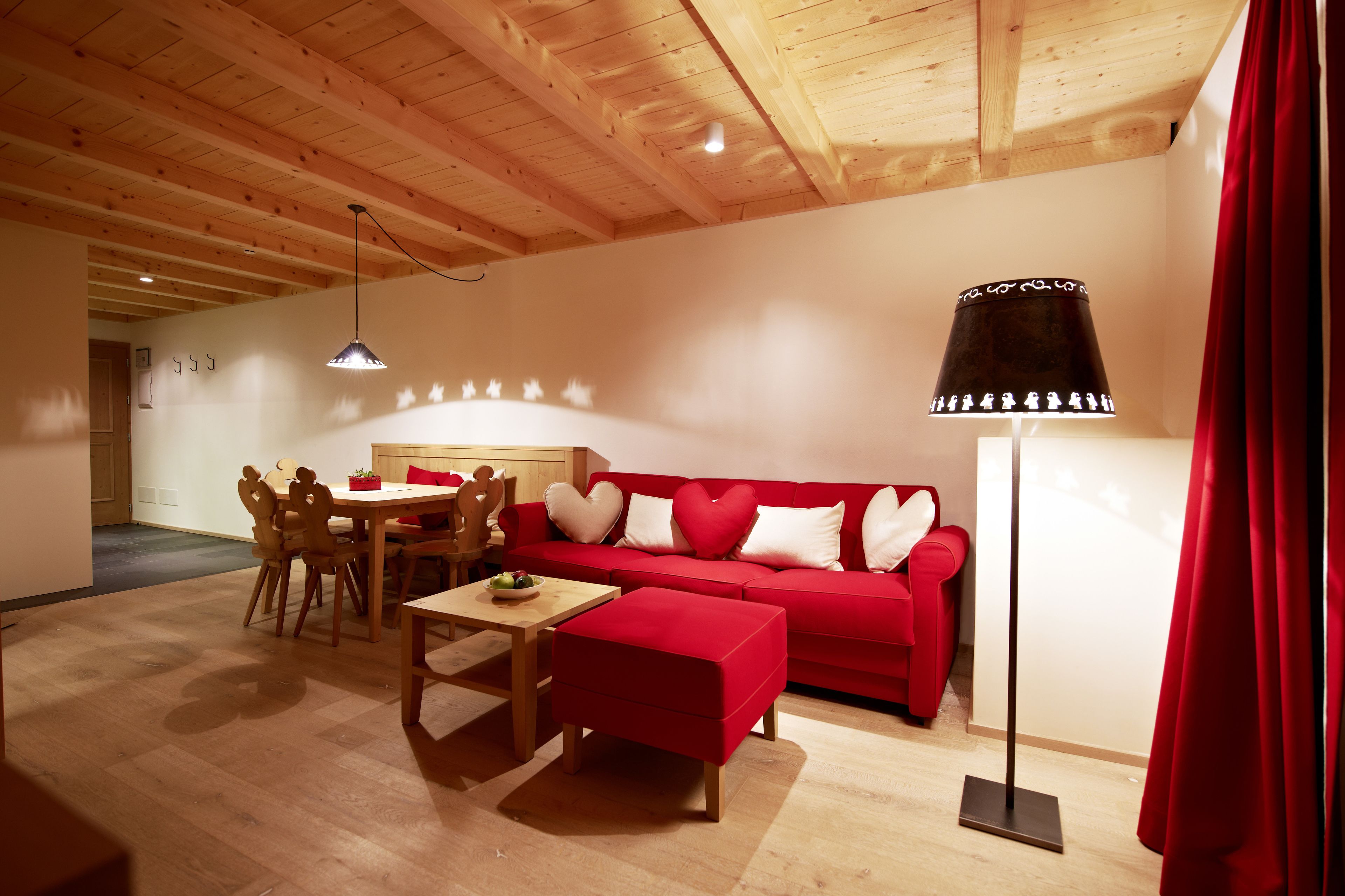 Un accogliente soggiorno con un divano rosso, travi in legno a soffitto, un tavolo da pranzo con sedie e una lampada da terra.