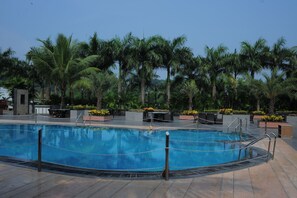 A swimming pool surrounded by palm trees and outdoor seating areas. - Hotel Sea N Rock (Mumbai)