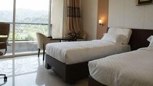 Habitación de hotel con dos camas, una silla, una mesa y vistas al exterior.