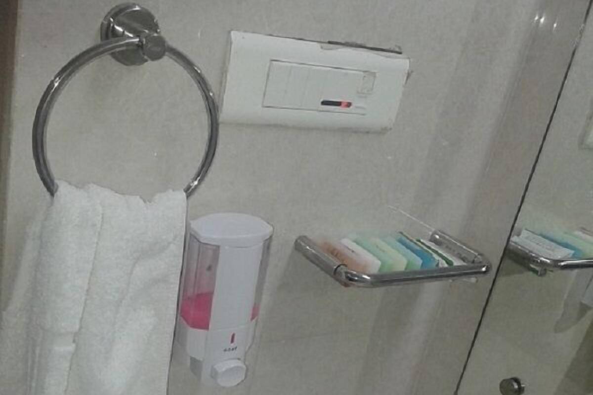 A bathroom with a toilet, a sink, a mirror, a towel ring, a soap dispenser, and a toothbrush holder.