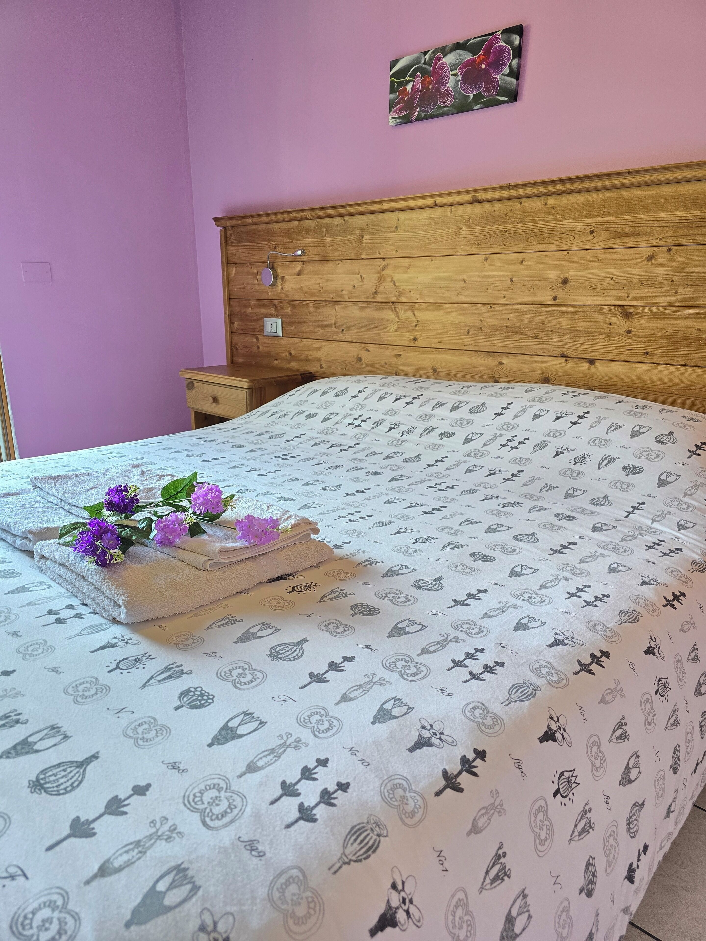 A neatly made bed with a floral-patterned bedspread, a wooden headboard, and a small bedside table with a lamp.