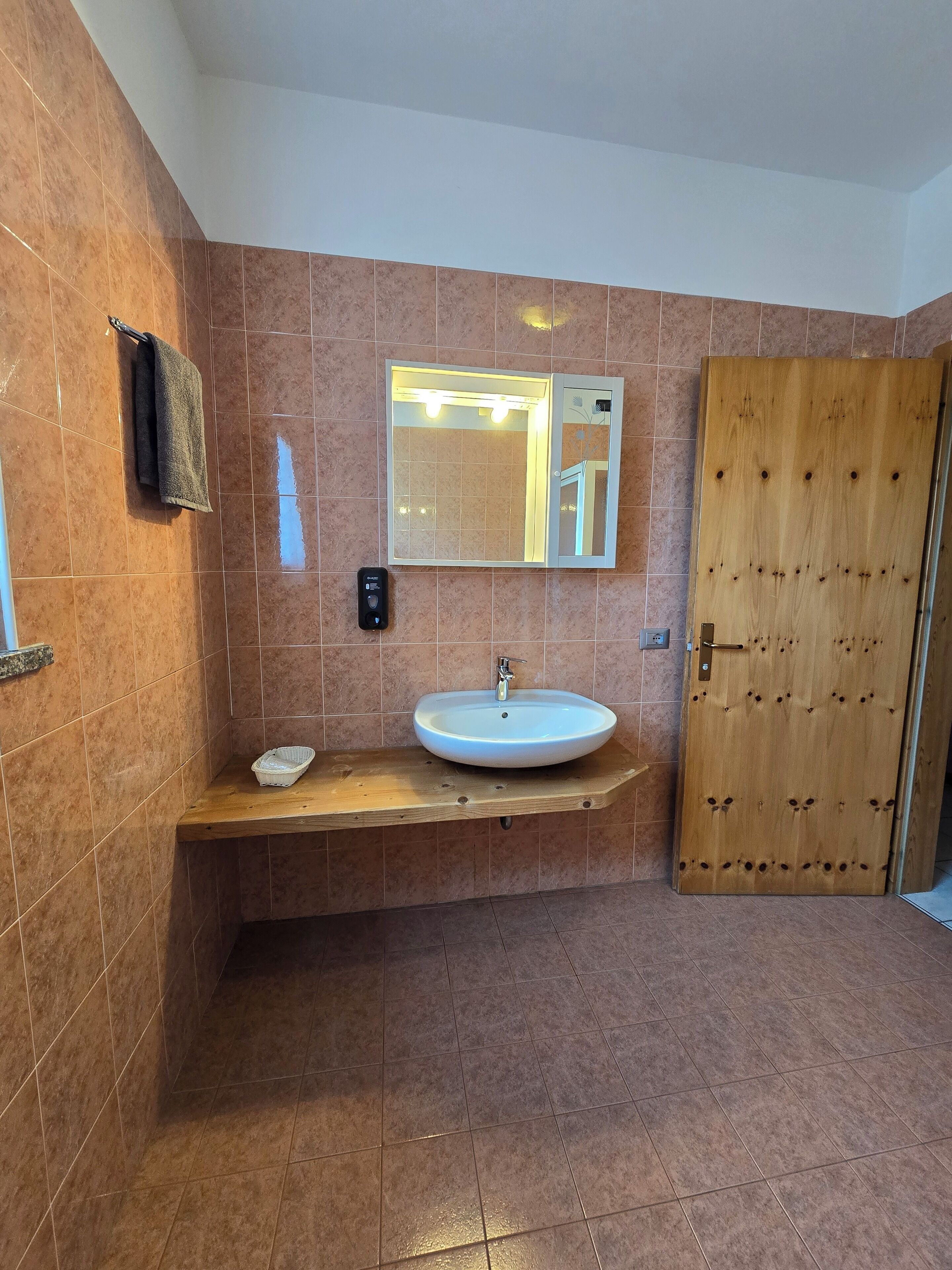 Un baño con tocador de madera, un lavabo blanco, un espejo y una puerta de madera.