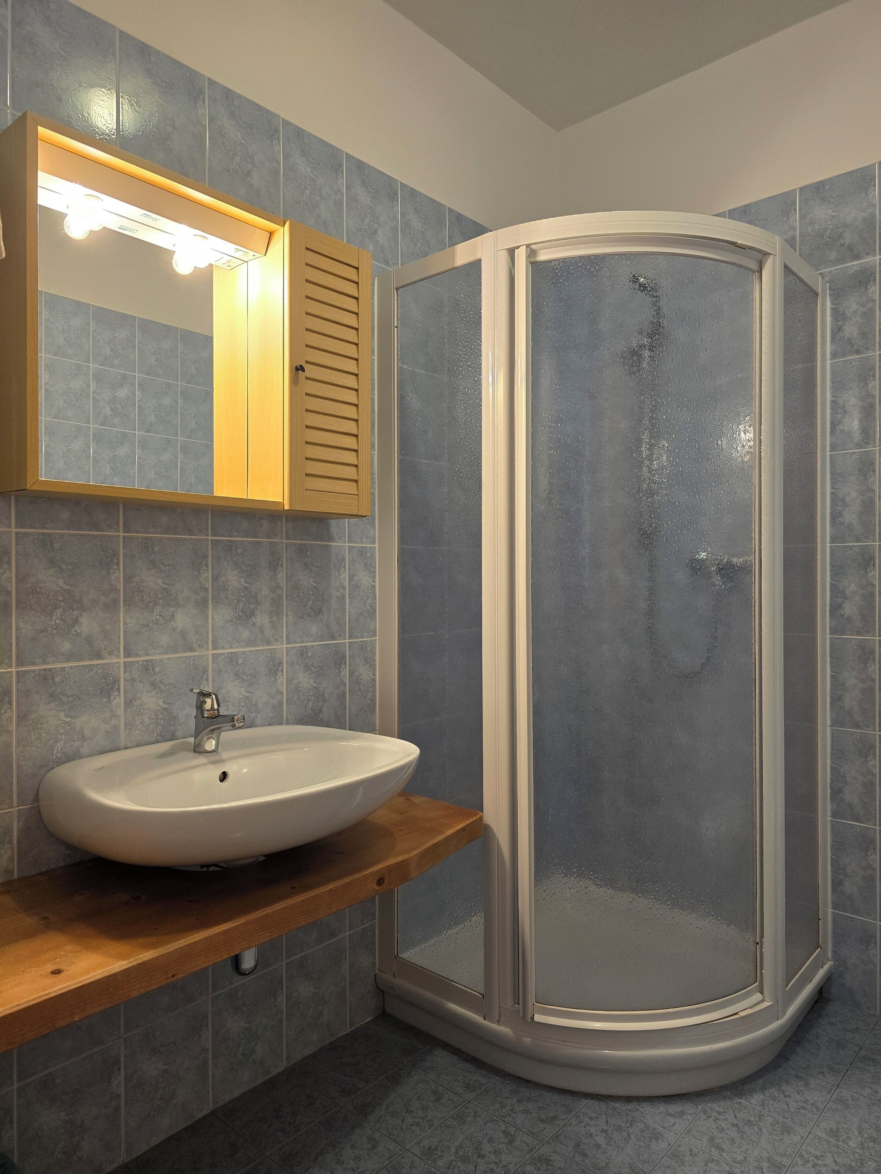 A bathroom with a white sink, a mirror with lights, and a glass-enclosed shower.