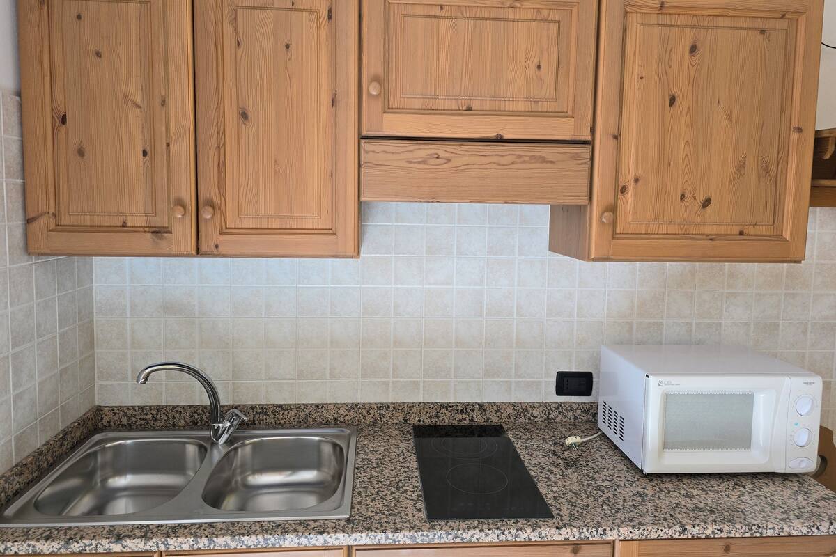 A kitchen with wooden cabinets, a stainless steel sink, a microwave, and a granite countertop.