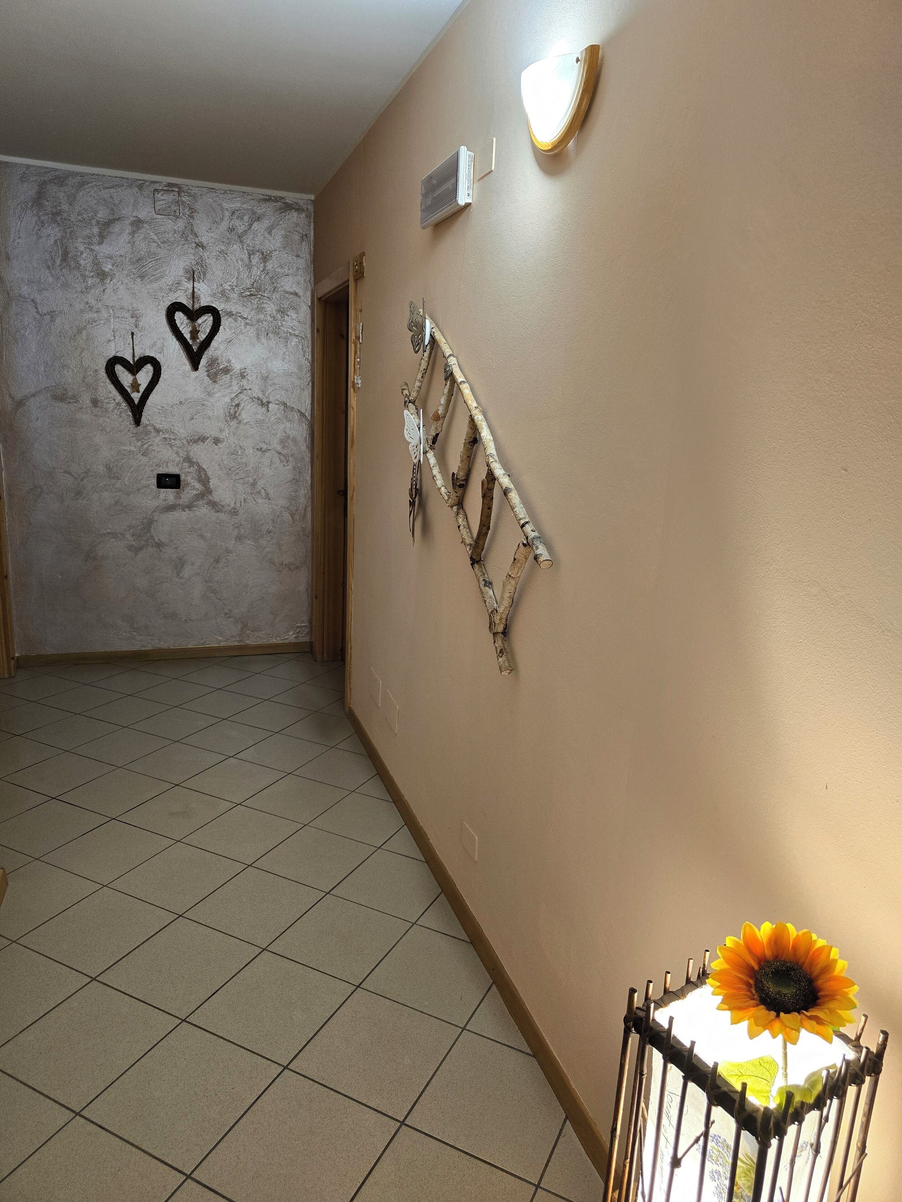 Un pasillo con suelo de baldosas, pared decorada con una rama y una mariposa, y una puerta con interruptor de luz.