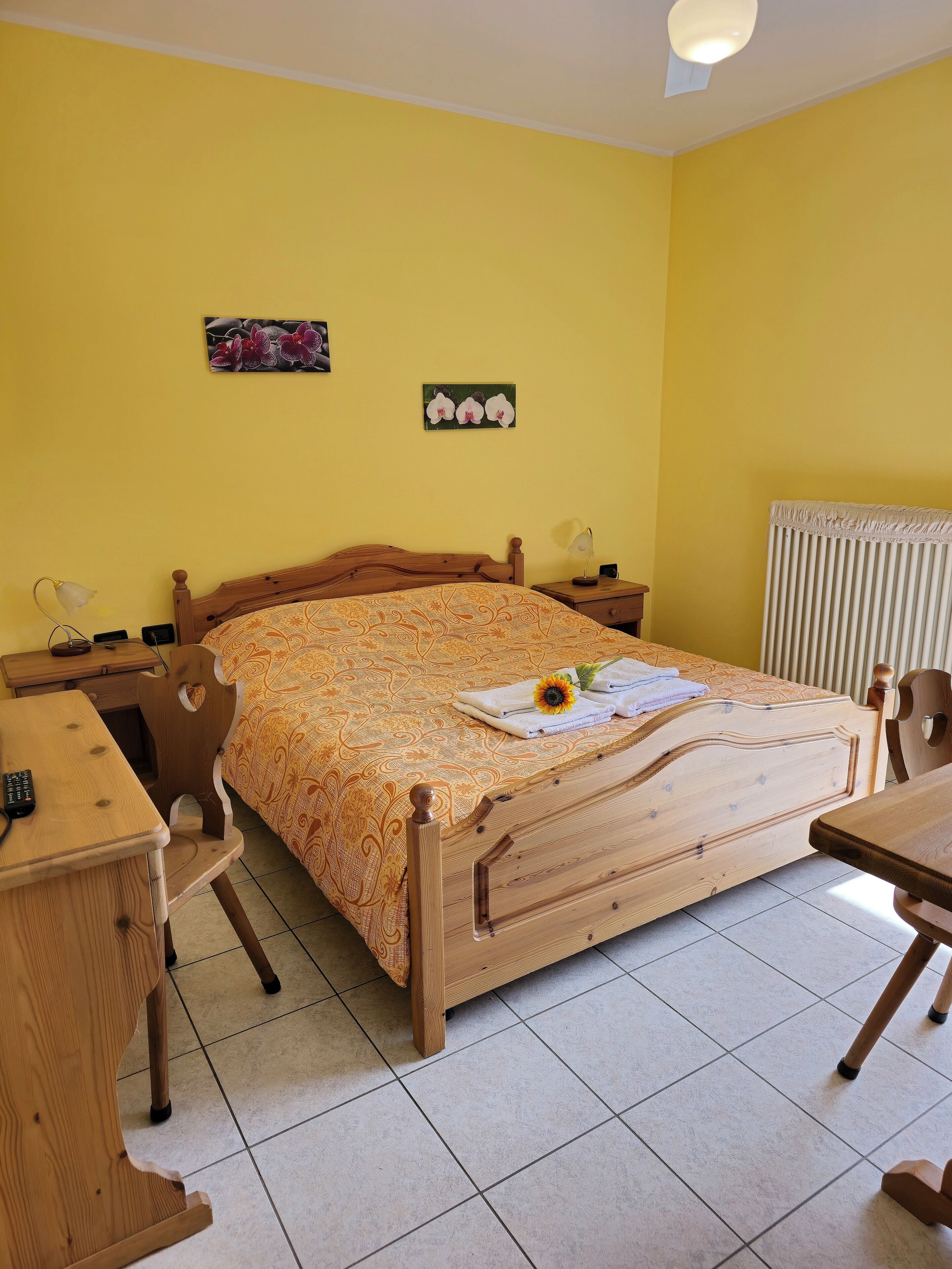 Un dormitorio con cama de madera, escritorio, silla, mesita de noche y radiador.