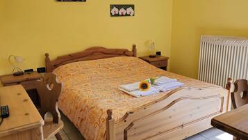 A bedroom with a wooden bed, a desk, a chair, a bedside table, and a radiator.