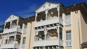 Un edificio de varios pisos con fachada simétrica, con balcones y barandillas ornamentales y una entrada central con un frontón decorativo.