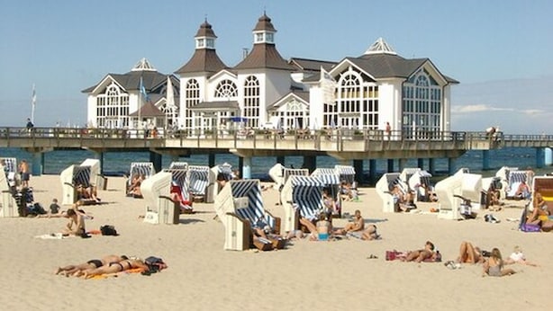 Una playa con un edificio blanco grande, con múltiples torres y un muelle que se adentra en el agua.
