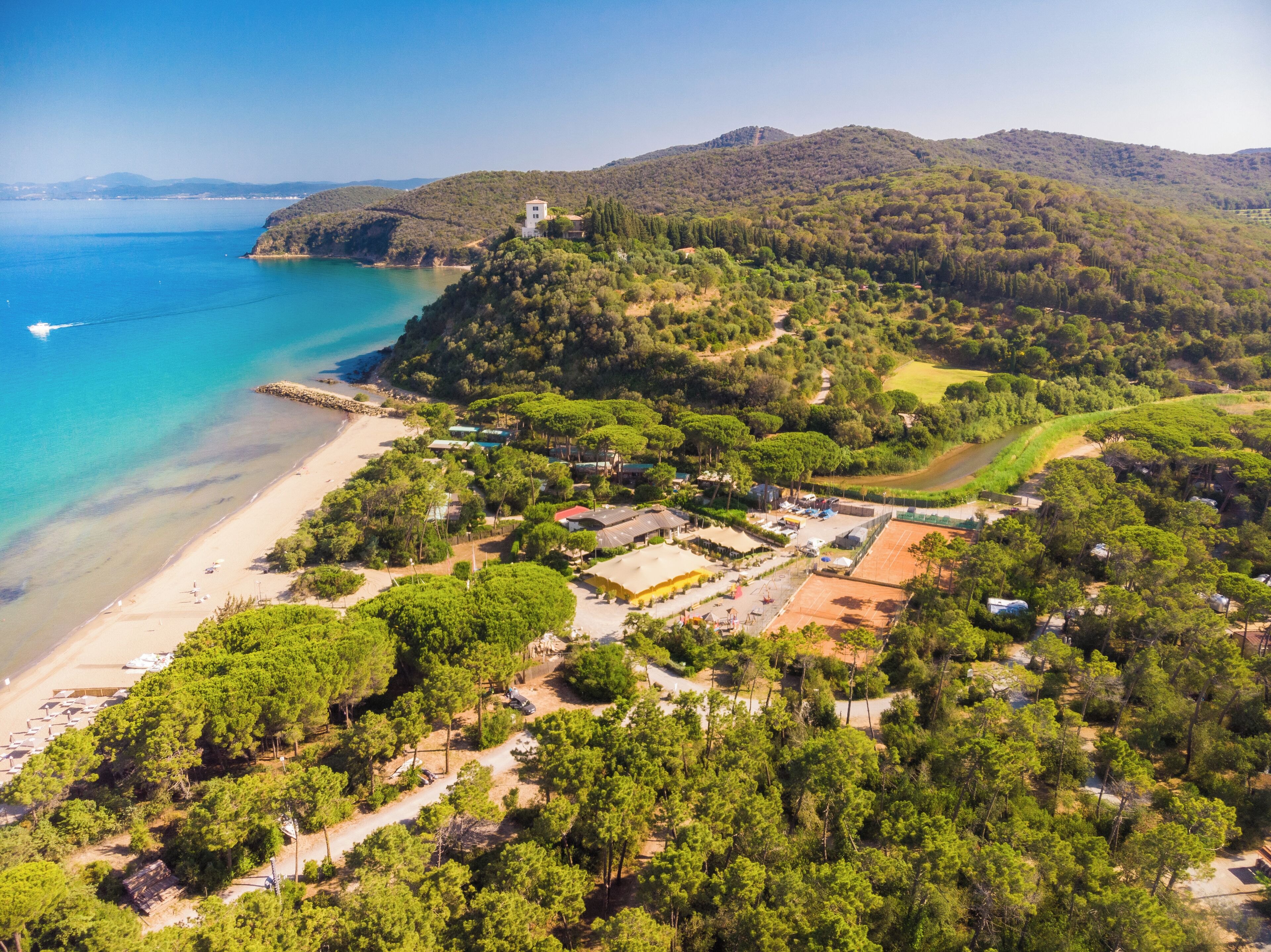 An aerial view of a coastal area with a beach, a small hill with a building, and a clear sky.