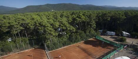 A tennis court surrounded by dense forest and mountains.
