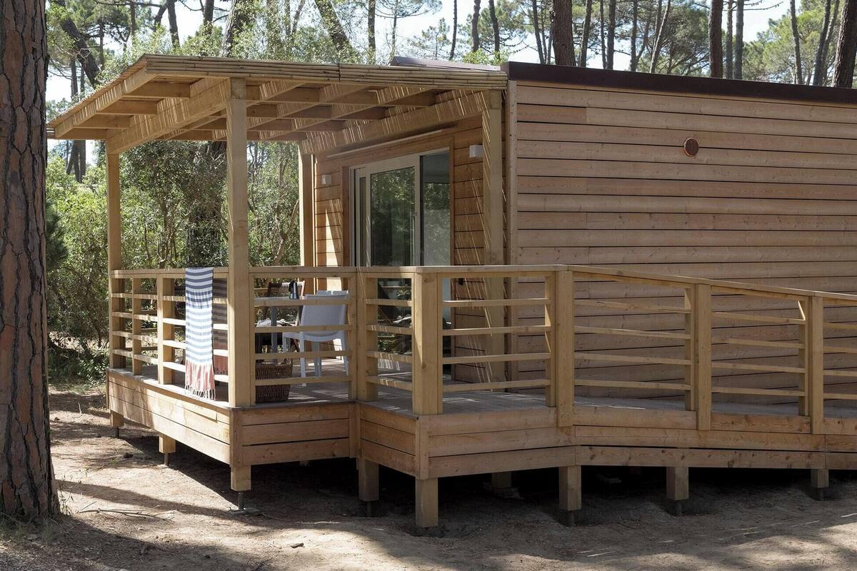 Een houten chalet met een overdekte veranda, een eethoek met stoelen en een tafel, en een raam.