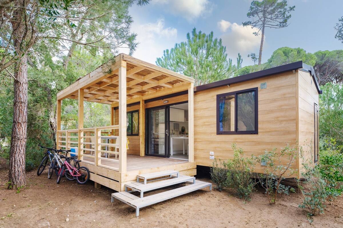 Een houten hut met een overdekte veranda, een keukenhoek en een klein zitgedeelte buiten.
