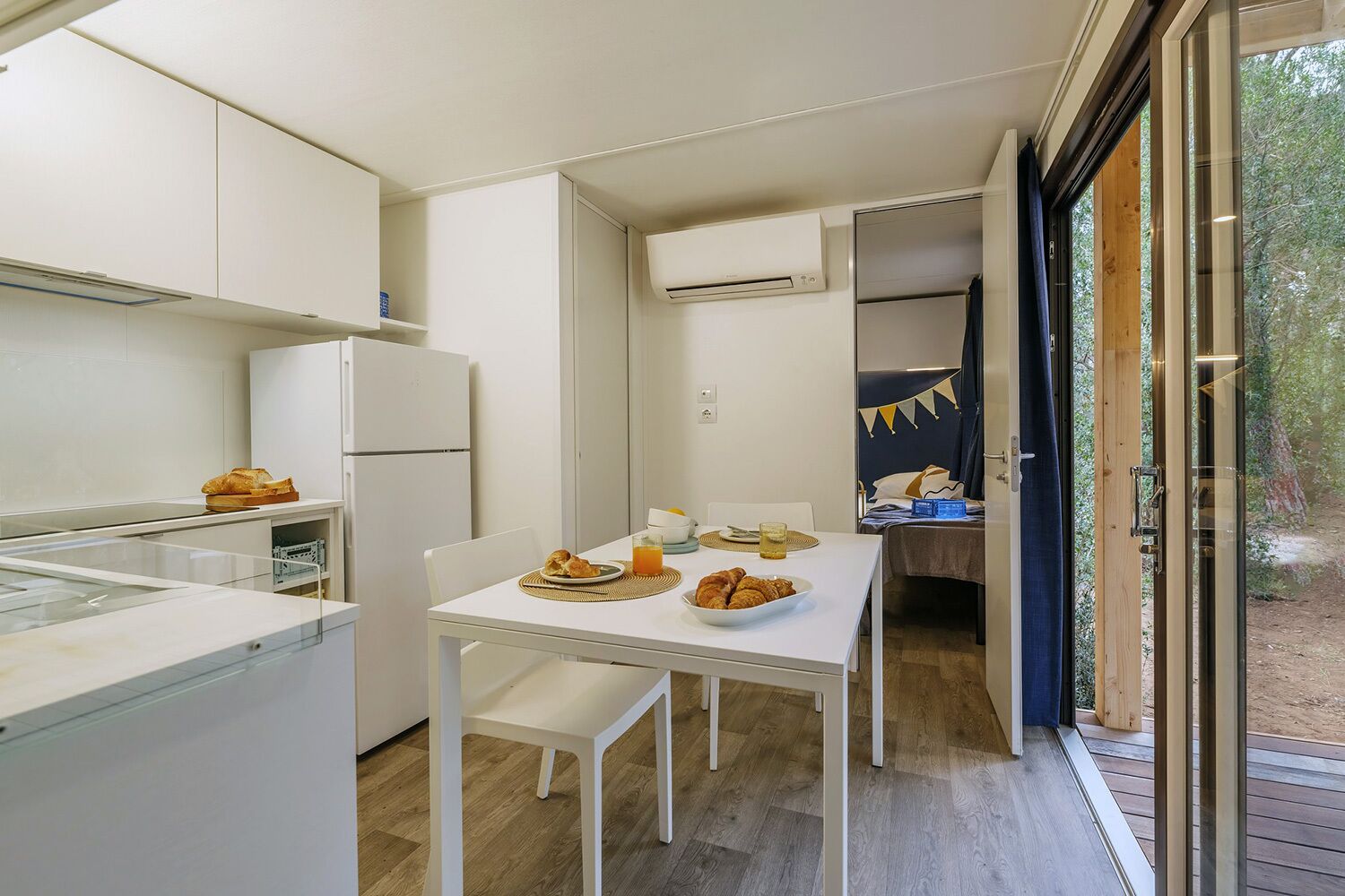 A compact kitchen with a dining area, a refrigerator, and a table set with food and drinks.