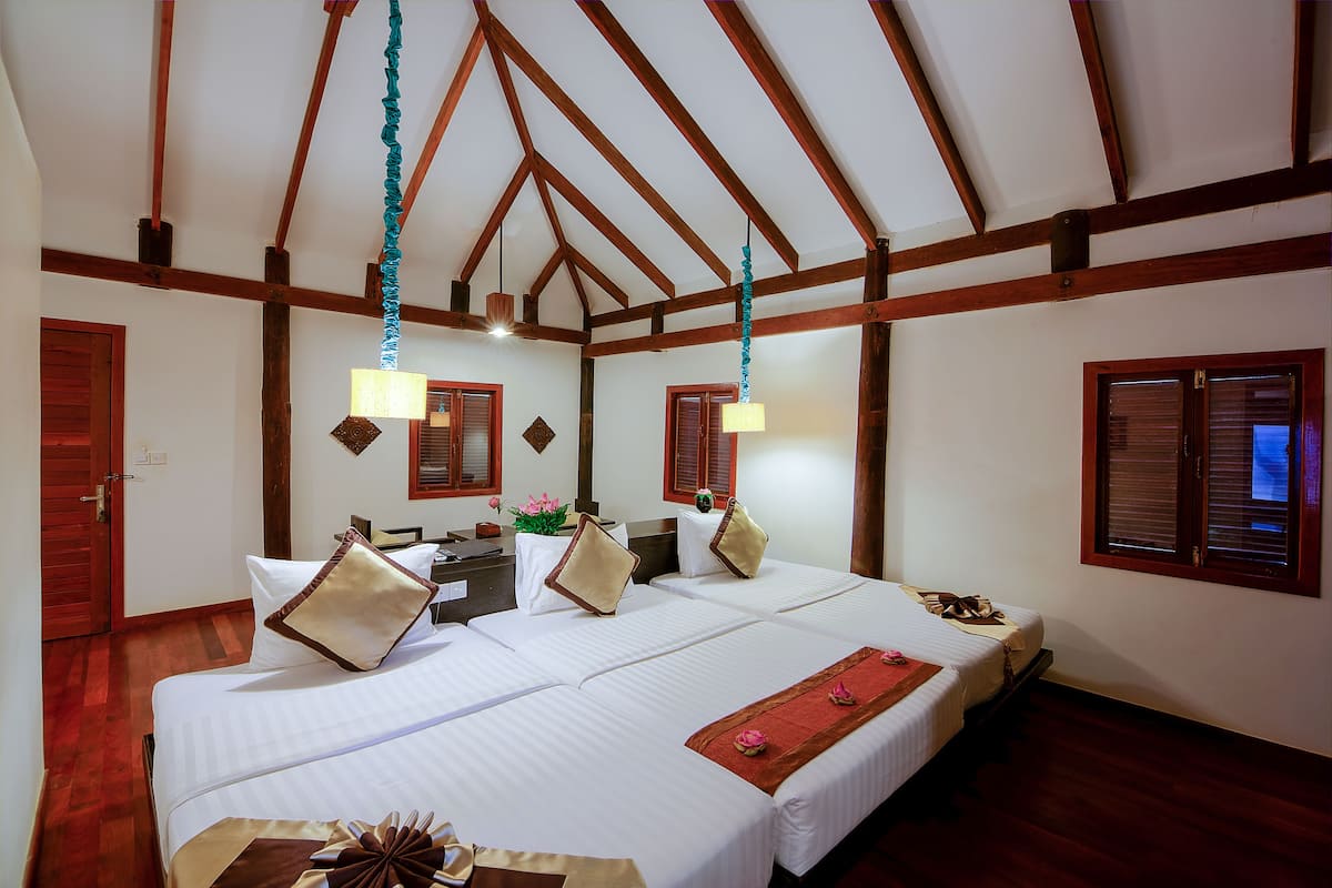 Habitación de hotel con dos camas, vigas de madera en el techo, un escritorio con lámpara y una ventana con contraventanas.