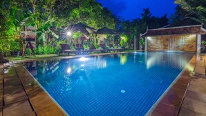 A swimming pool with lounge chairs and umbrellas, surrounded by lush greenery and a small pavilion. - Bunwin Residence (Siem Reap)